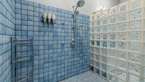 A bathroom with blue tiled walls, a shower with a handheld showerhead, and a glass shower enclosure. - The Residence at Freshwater Bay (Port Angeles)