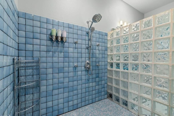 Ein Badezimmer mit blauen Fliesen, einer Dusche inklusive Handbrause und einer Duschkabine aus Glas.