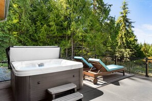 Ein Whirlpool mit Holzterrasse, Liegestühlen und Blick auf ein bewaldetes Gebiet.