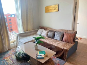 A modern living room with a sofa, coffee table, and a view of a cityscape. - #164 Coral retreat in Birmingham CC -Sleeps 6 (West Midlands)