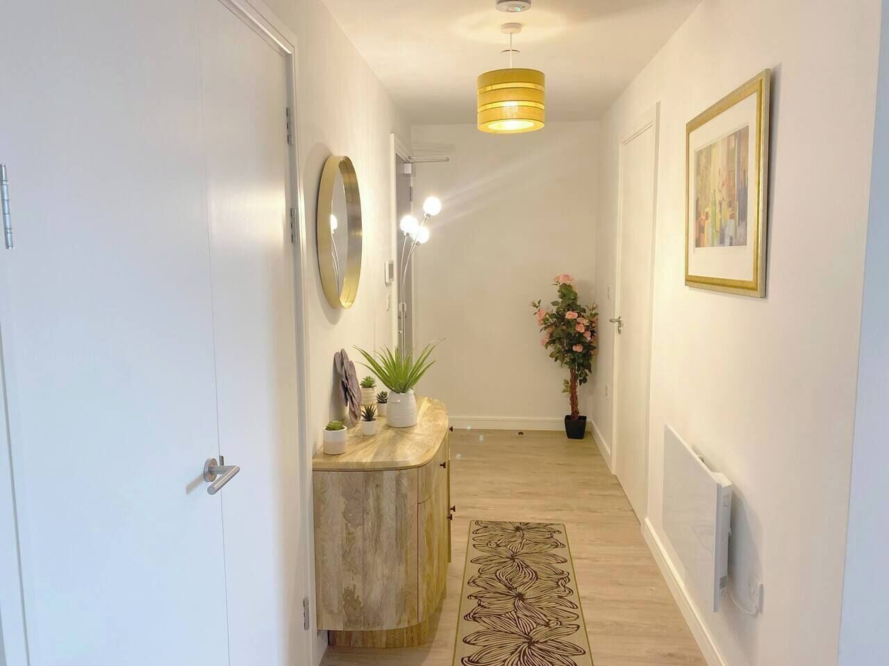 A hallway with a wooden cabinet, a mirror, a potted plant, a rug, and a ceiling light fixture.