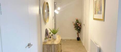 Un couloir avec une armoire en bois, un miroir, une plante en pot, un tapis et un luminaire au plafond.