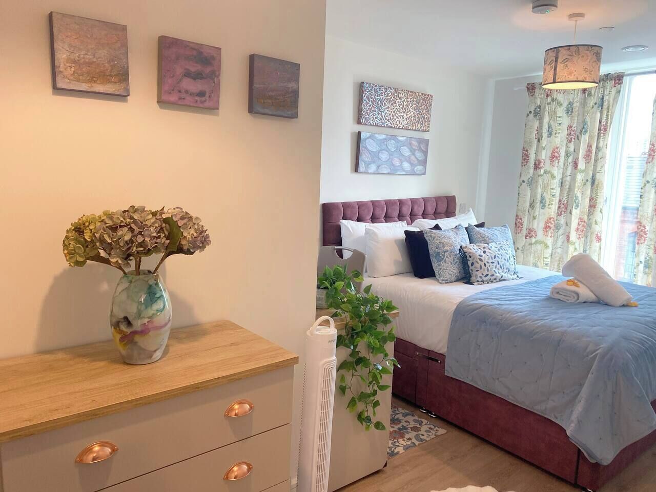 A bedroom with a bed, bedside table, and a vase with flowers.