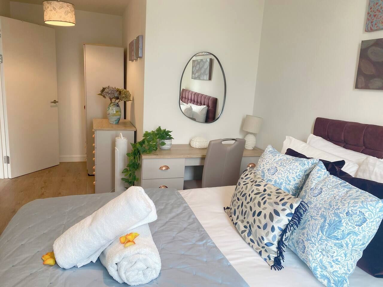 Une chambre d’hôtel avec un lit, un bureau, une chaise, un miroir et une plante.