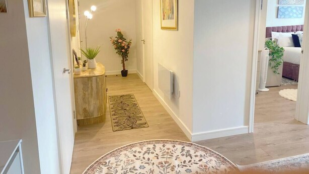 A hallway with a wooden floor, a round rug, a potted plant, and a wall-mounted light fixture. - #164 Coral retreat in Birmingham CC -Sleeps 6 (West Midlands)