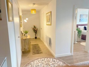 A hallway with a wooden floor, a round rug, a potted plant, and a wall-mounted light fixture. - #164 Coral retreat in Birmingham CC -Sleeps 6 (West Midlands)