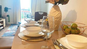 A dining table set with plates, bowls, cutlery, and wine glasses, with a vase of flowers and a fruit bowl on the table. - #164 Coral retreat in Birmingham CC -Sleeps 6 (West Midlands)