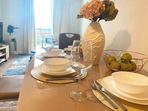 A dining table set with plates, bowls, cutlery, and wine glasses, with a vase of flowers and a fruit bowl on the table. - #164 Coral retreat in Birmingham CC -Sleeps 6 (West Midlands)