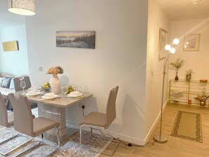 A dining area with a table set for four, chairs, a vase with flowers, and a painting on the wall. - #164 Coral retreat in Birmingham CC -Sleeps 6 (West Midlands)