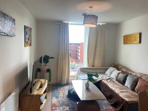 Un salon moderne avec un canapé, une table basse, un téléviseur et une grande fenêtre avec des rideaux.