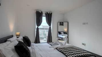 A hotel room with a bed, a checkered throw, a swan-shaped towel, a lamp, and a window with curtains.