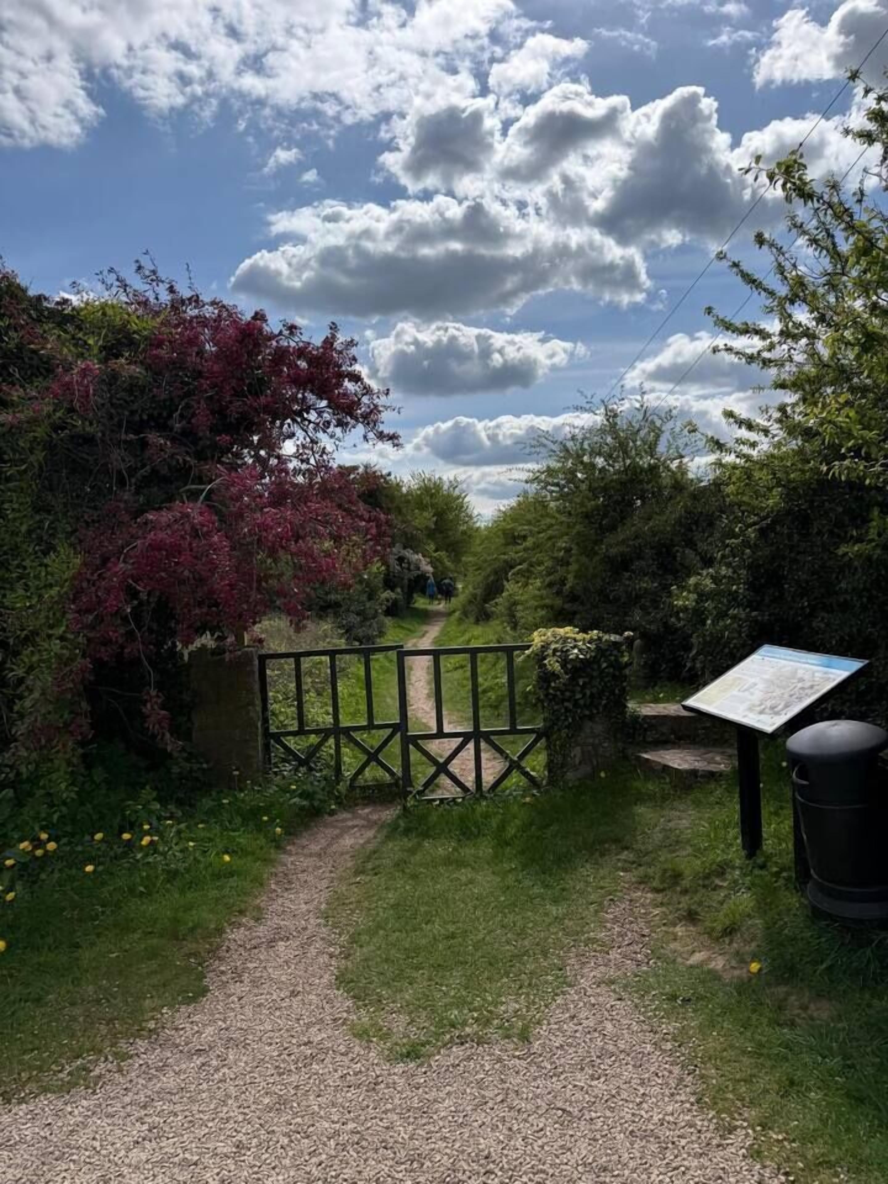 A gravel path leading to a gated entrance surrounded by greenery and a clear sky.