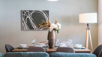 A dining area with a table set for four, a vase with flowers, a floor lamp, and a piece of abstract art on the wall.