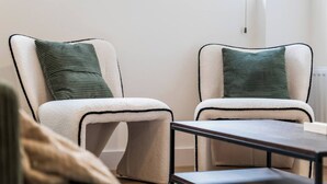 Two chairs with a white and black frame, a green pillow, and a small table in a room with a white wall and a window.