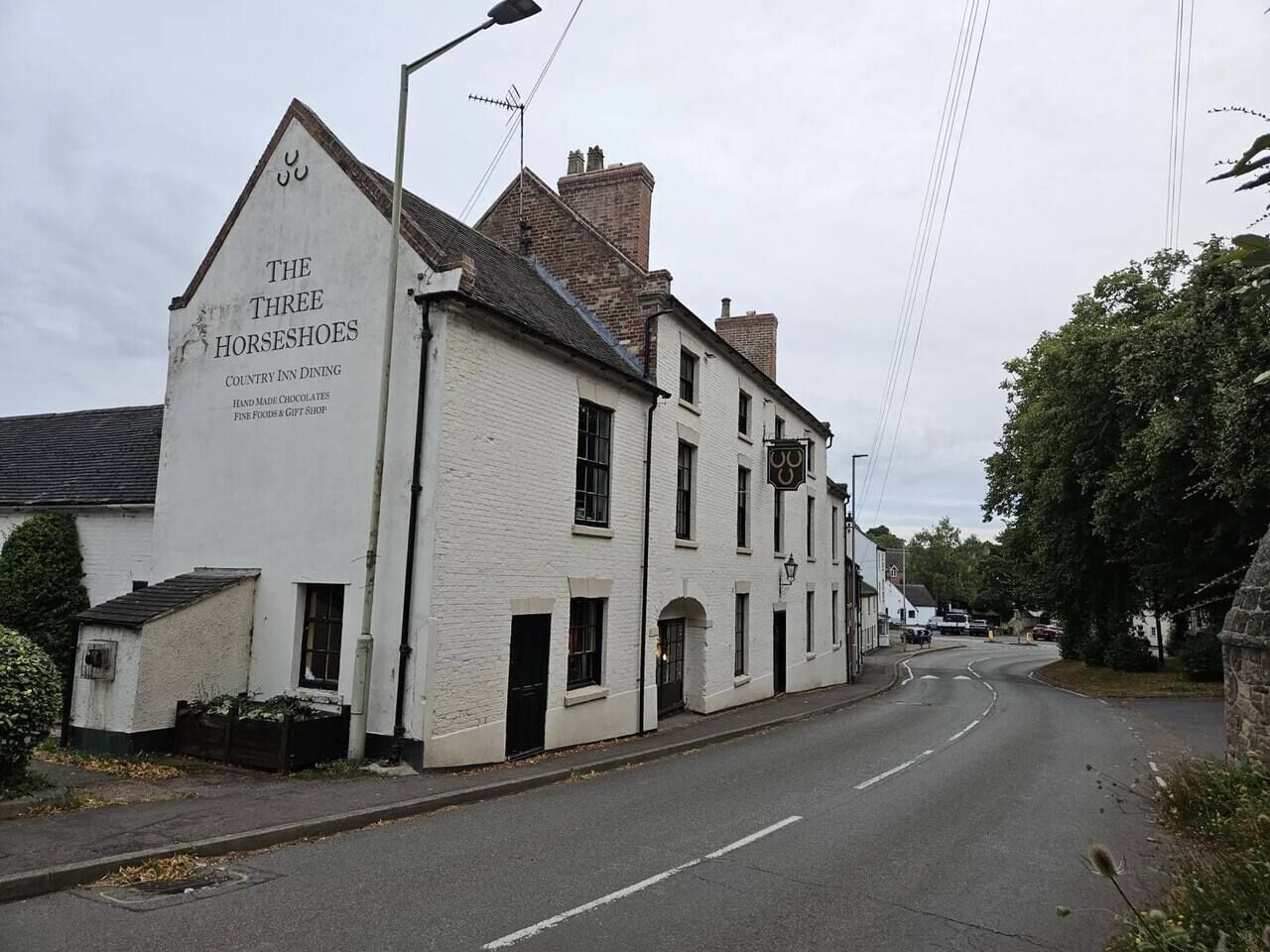 A white building with a sign for 'The Three Horseshoes' which is a country inn offering dining, handmade chocolates, fine foods, and a gift shop.