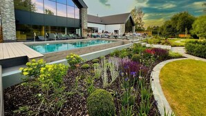 A modern building with a swimming pool, surrounded by landscaped gardens and a clear sky.