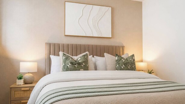 A bedroom with a bed, pillows, a nightstand, a lamp, and a wall art piece.