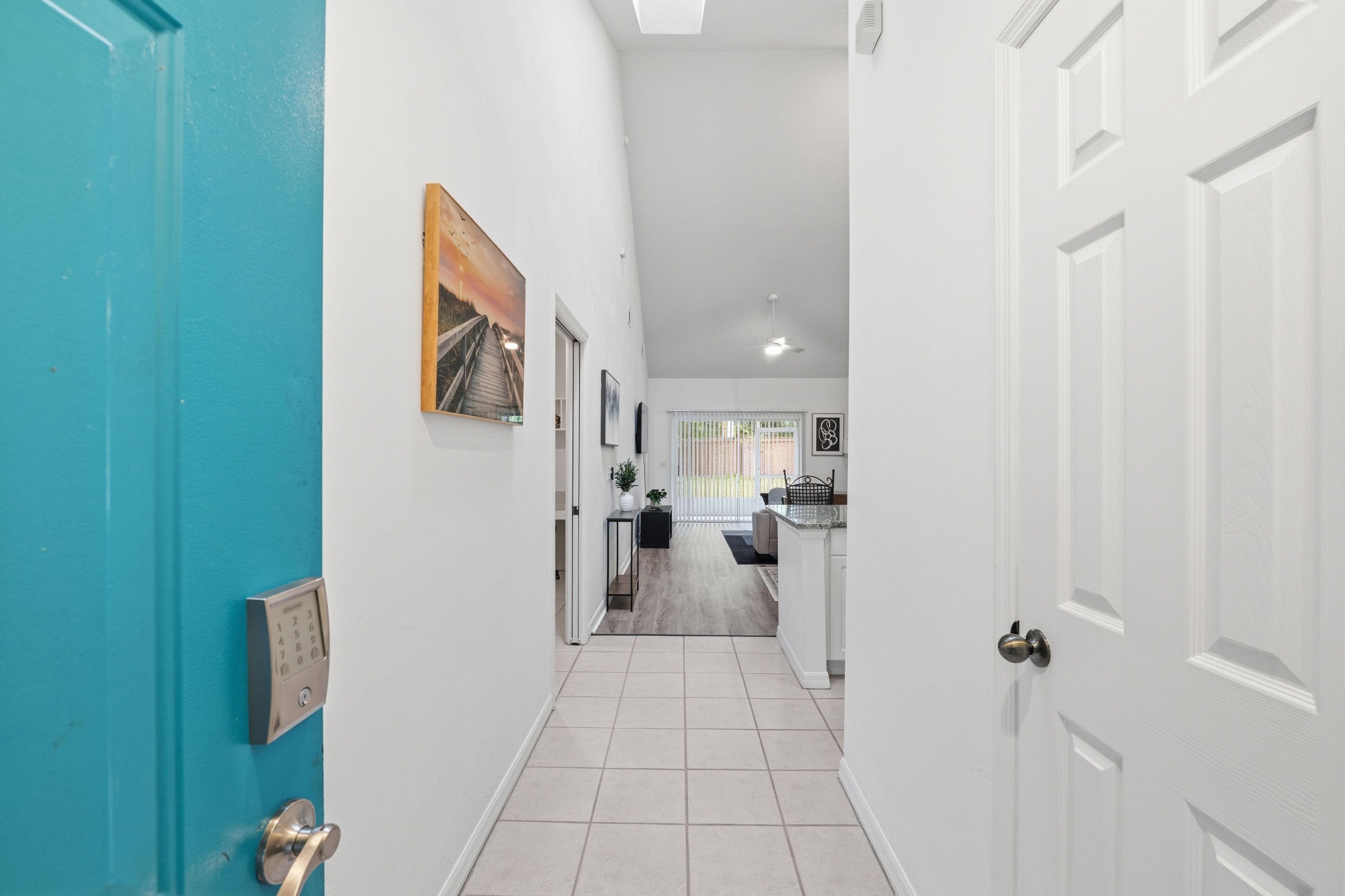 A hallway with a blue door, a white door, and a view into a kitchen area.