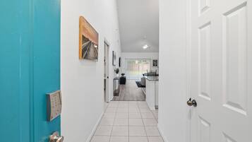 A hallway with a blue door, a white door, and a view into a kitchen area.