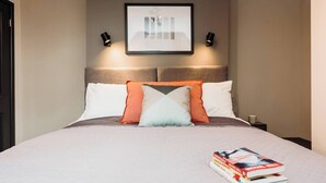 A neatly made bed with a variety of pillows, a framed picture on the wall, and a stack of books on the side. - #44 Victoria Apartment3|near snowdome| Guest for 4 (Staffordshire)