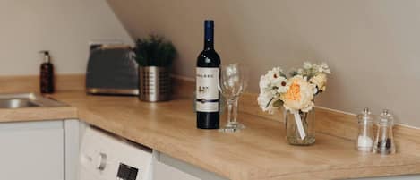 Una encimera de cocina con una botella de vino, copas y un florero con flores.