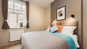 A bedroom with a bed, a window with curtains, a radiator, and a wall-mounted picture.