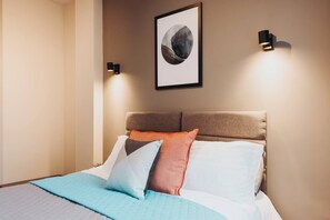 Una habitación de hotel con una cama, cabecera y dos lámparas fijadas a la pared.