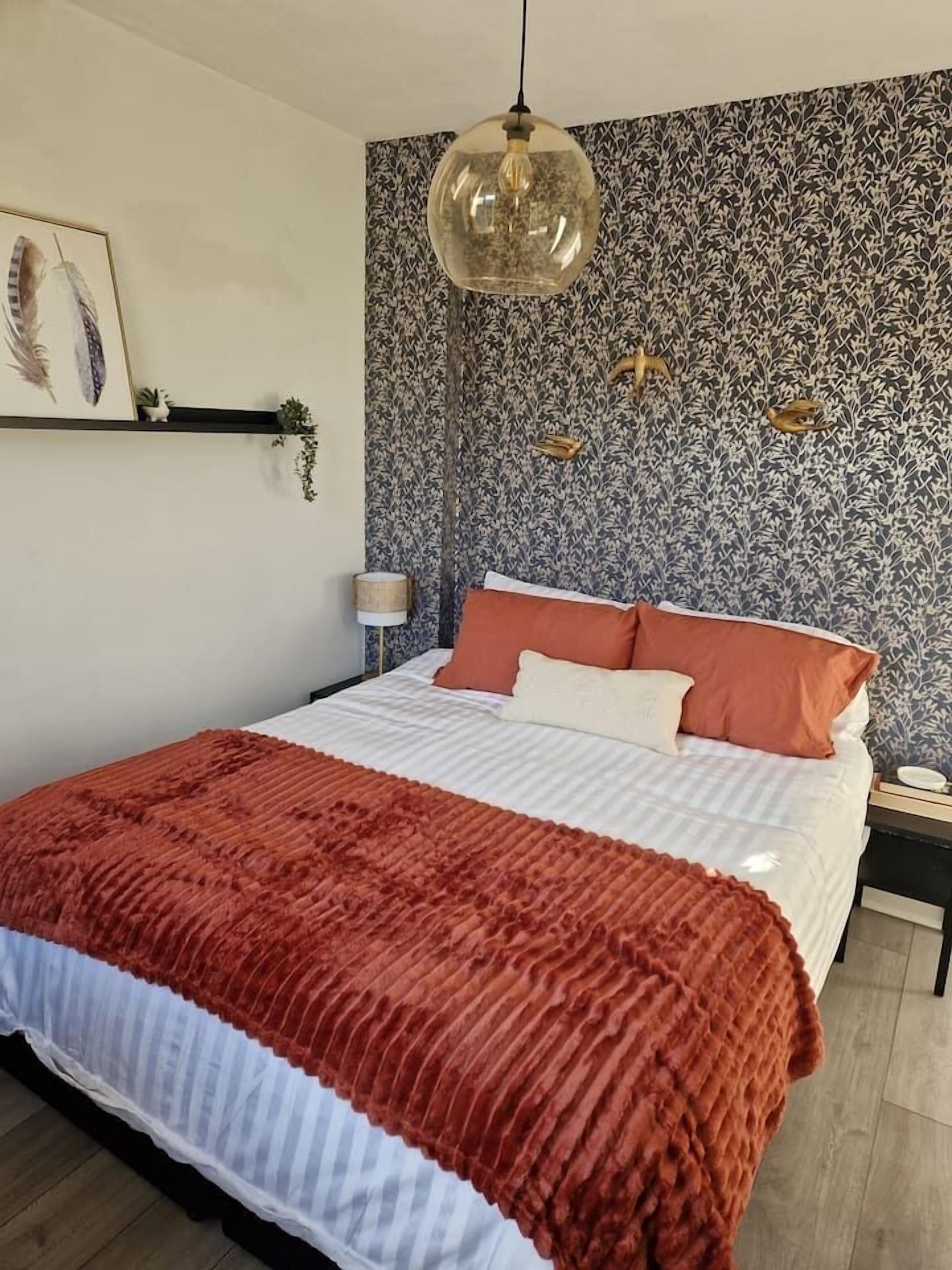 A bedroom with a bed, a hanging light fixture, and a patterned wall.