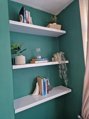 Eine türkis gefärbte Wand mit drei weißen Regalen, auf denen Bücher, Dekorationen und je ein Topfpflanzen stehen.