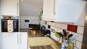 Eine kleine Küche mit weißen Schränken, einer Mikrowelle, einem Toaster und einem Holzer Schneidebrett.
