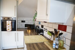 A compact kitchen with white cabinets, a microwave, a toaster, and a wooden cutting board. - Coventry Home: Playroom & CBS Arena (West Midlands)