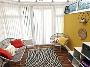 A room with a wicker sofa, a chair, a patterned rug, and a bookshelf. - Coventry Home: Playroom & CBS Arena (West Midlands)