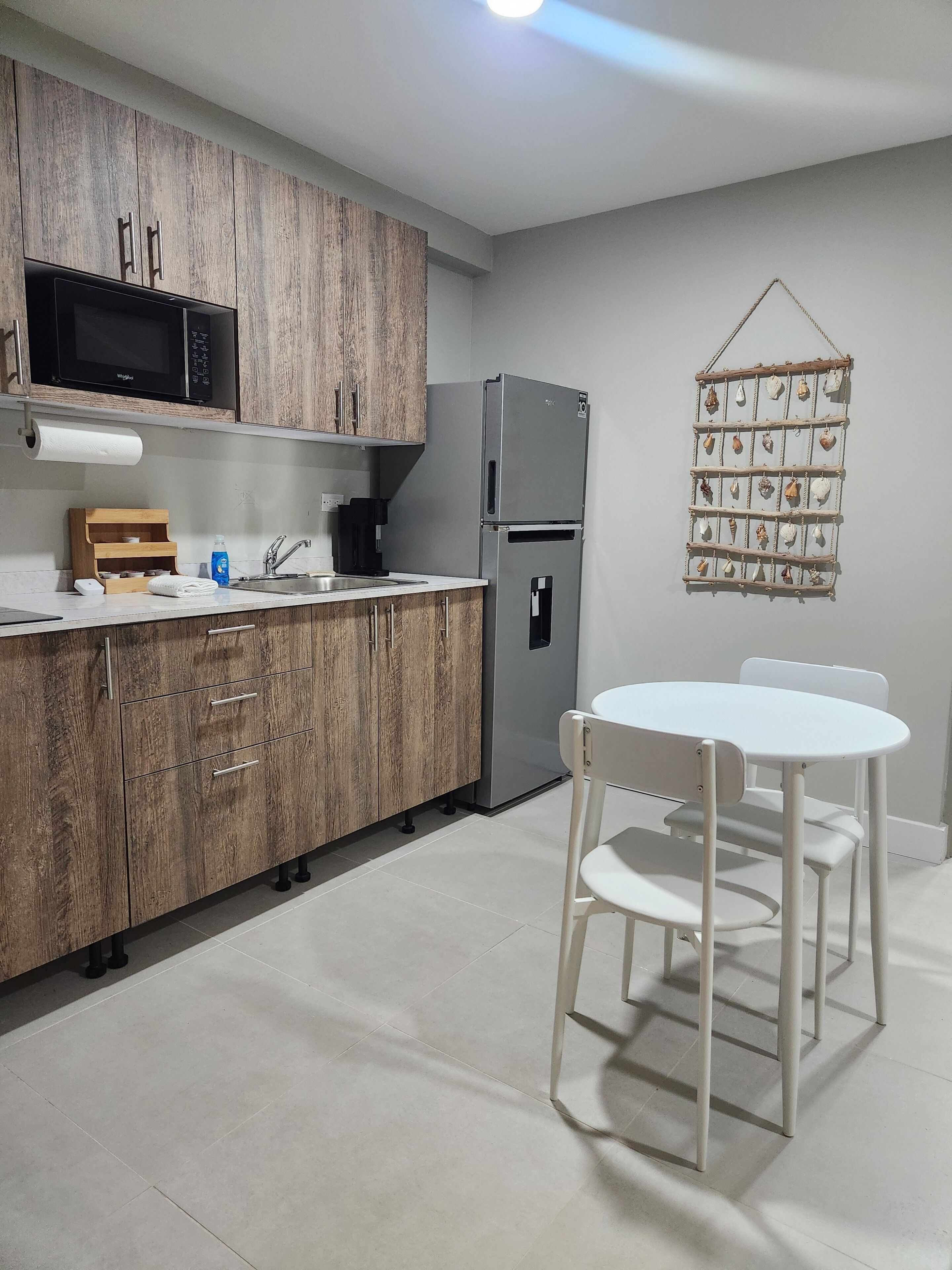 A modern kitchen with wooden cabinets, a stainless steel refrigerator, a microwave, and a white dining table with chairs.