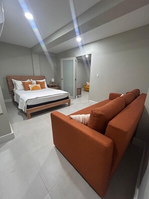 Un dormitorio con cama, sofá, mesita de noche y una puerta que da a otra habitación.