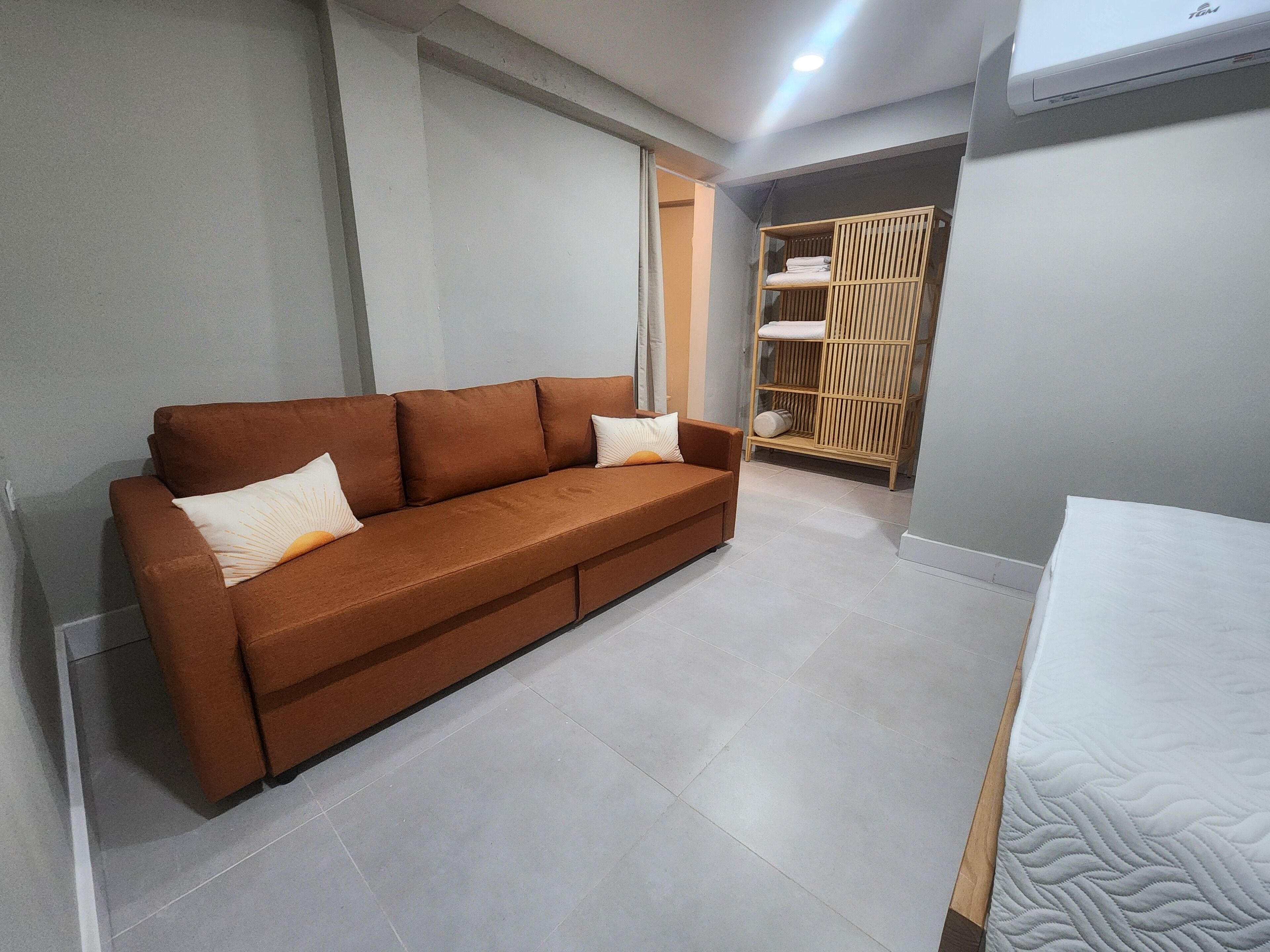 A room with a brown sofa, a wooden wardrobe, and a bed with a quilted mattress.