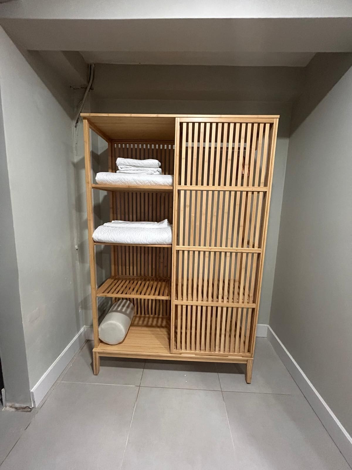 A wooden wardrobe with three shelves, a hanging rod, and a sliding door.