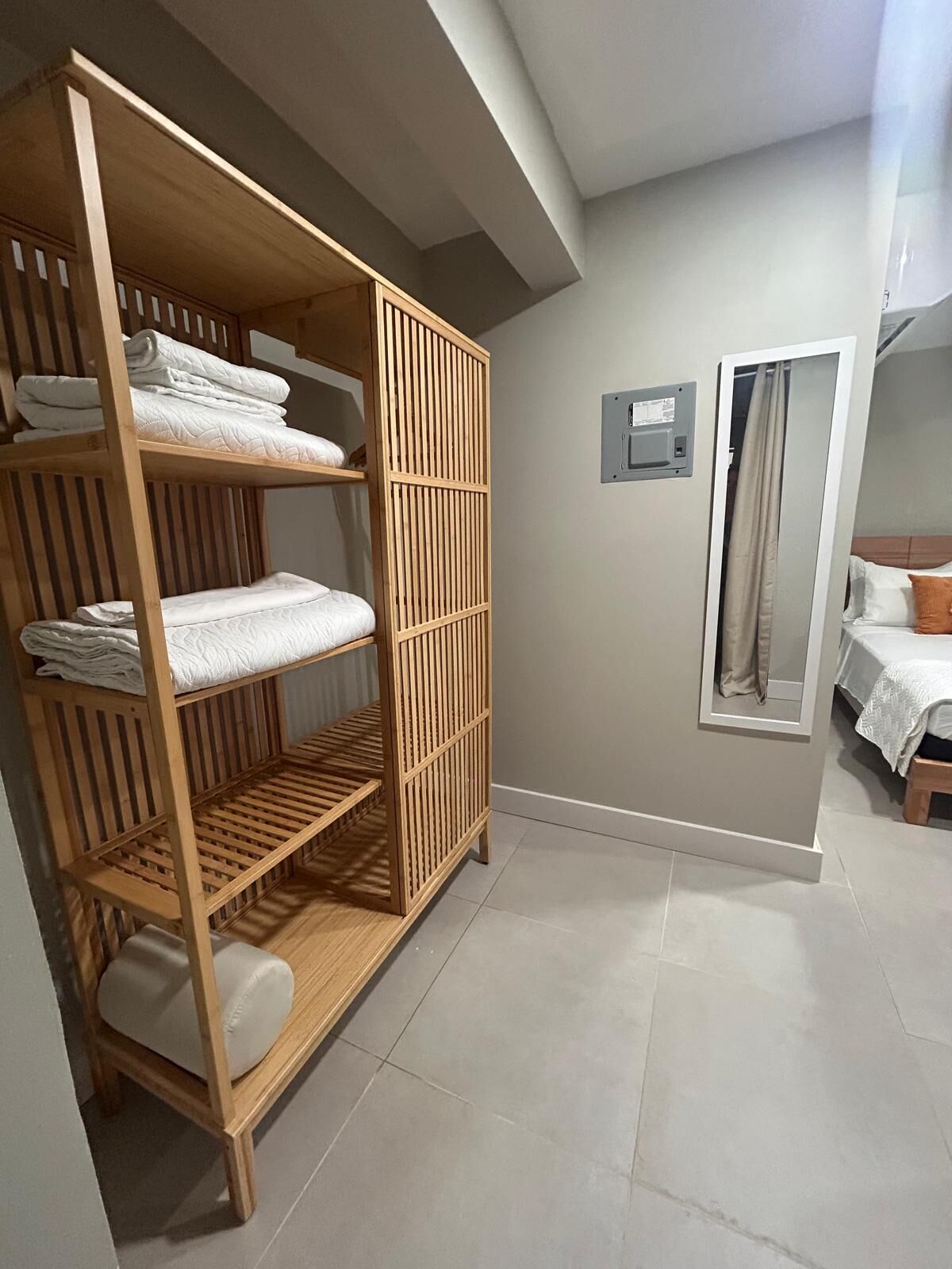 A room with a wooden wardrobe, a bed with a white duvet, and a mirror on the wall.
