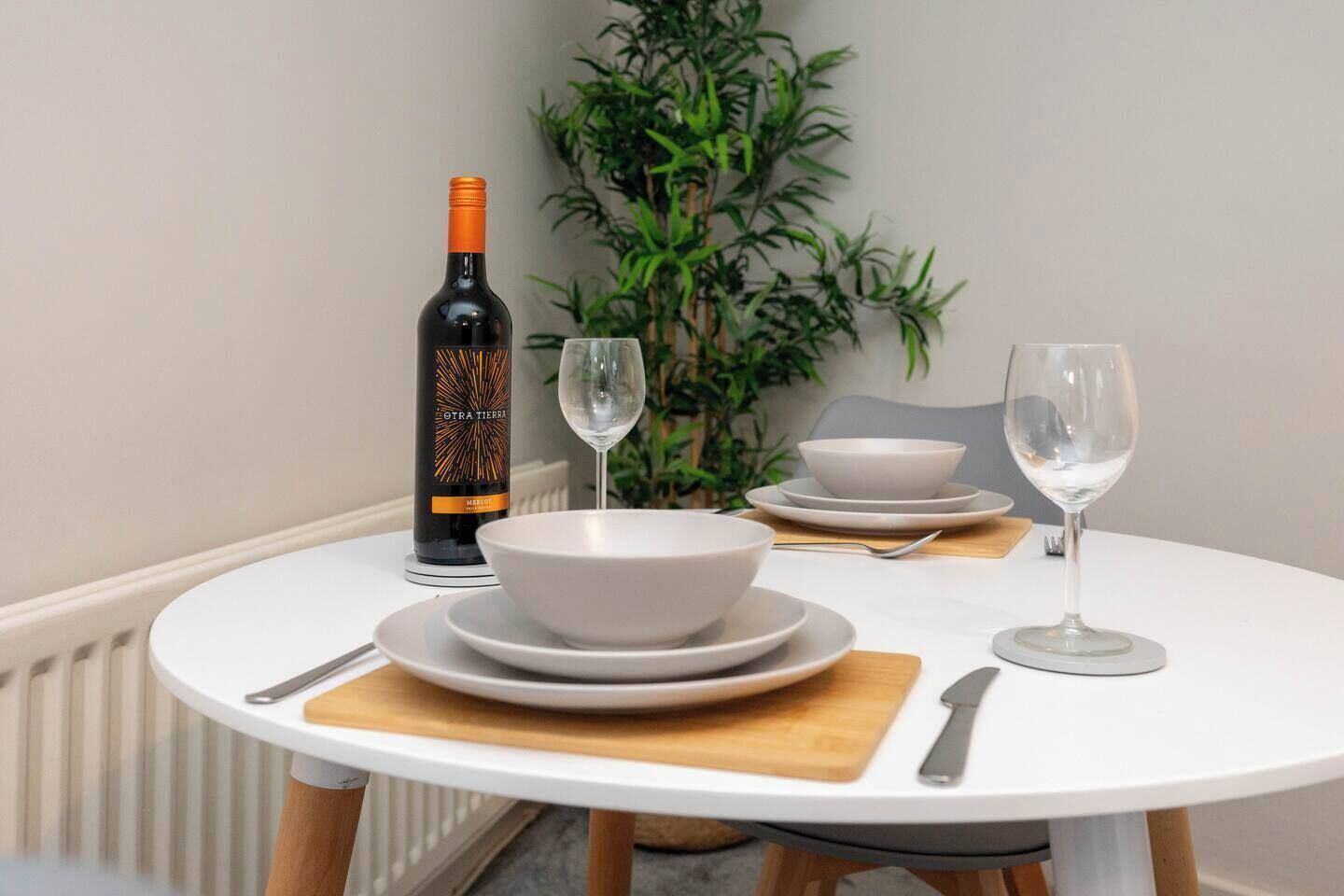 A dining table with a bottle of wine, two glasses, and white dinnerware.