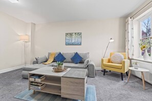 Ein modernes Wohnzimmer mit grauem Sofa, einem gelben Sessel, einem Couchtisch und einem Bücherregal.