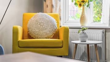 A yellow armchair with a patterned cushion, a small round table with a vase of sunflowers, and a radiator in the background.