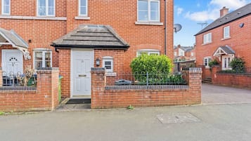 A red brick house with a white door, a small front garden, and a metal fence.