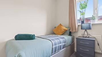 A bedroom with a bed, a nightstand, a lamp, and a window with curtains.