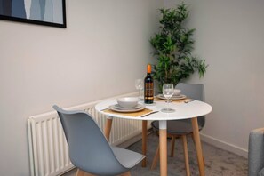 A dining area with a round table, chairs, a bottle of wine, and a bowl. - #33 Beautiful 2 bed apt Tamworth Private Parking (Two Gates)