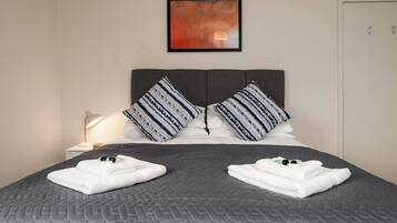 Una cama bien hecha con un edredón gris, dos almohadas con estampado a rayas y una lámpara de noche.