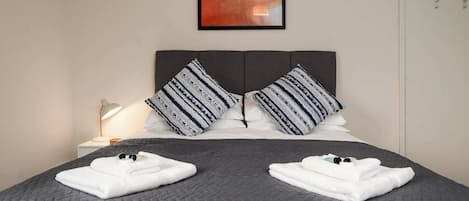 A neatly made bed with a grey quilt, two pillows with a striped pattern, and a bedside lamp.