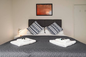 A neatly made bed with a grey quilt, two pillows with a striped pattern, and a bedside lamp. - #33 Beautiful 2 bed apt Tamworth Private Parking (Two Gates)
