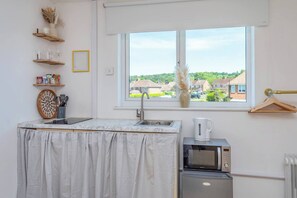 Eine kleine Küche mit Spüle, Wasserkocher und Mikrowelle. Ein Fenster bietet Blick auf Häuser und Grünflächen.