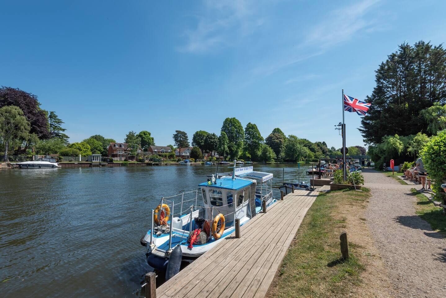 A river with boats docked, a wooden pier, and a flag.