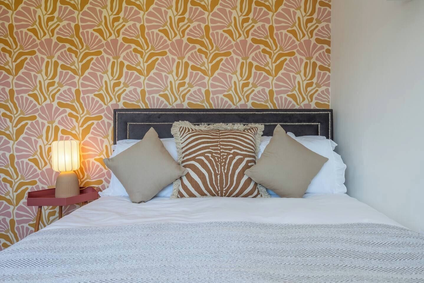 A bed with a headboard, pillows, and a bedside table with a lamp.