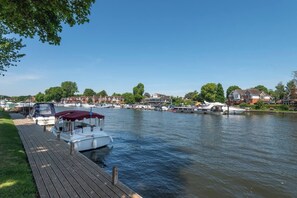 Ein ruhiger Fluss mit vertäuten Booten am Ufer, einem hölzernen Steg und Häusern im Hintergrund.